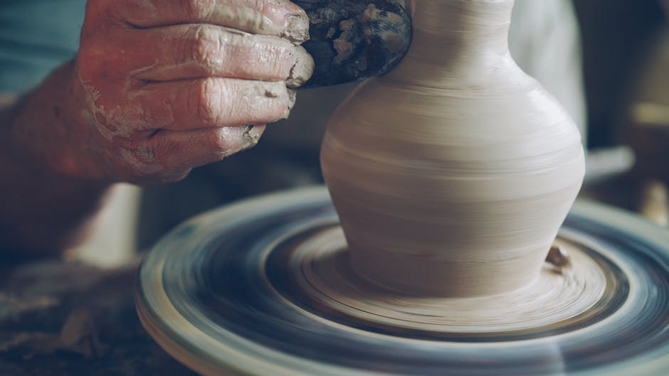 A potter skillfully shapes a ceramic vase on a spinning pottery wheel, focusing on detail.