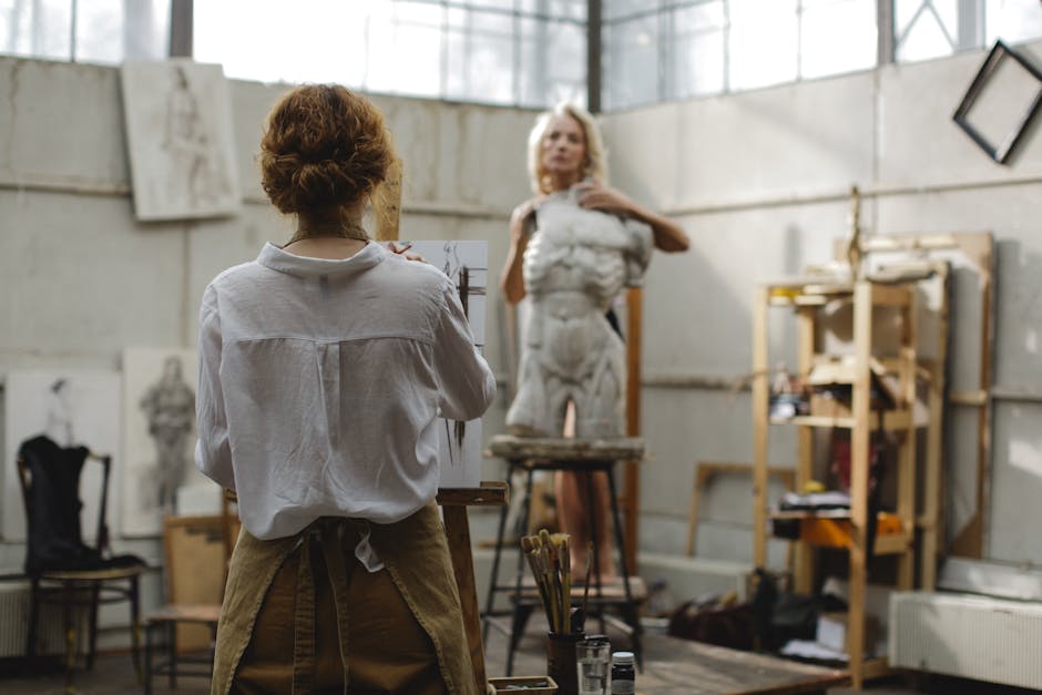 Artist at work painting a model posing near a sculpture in a well-lit art studio.