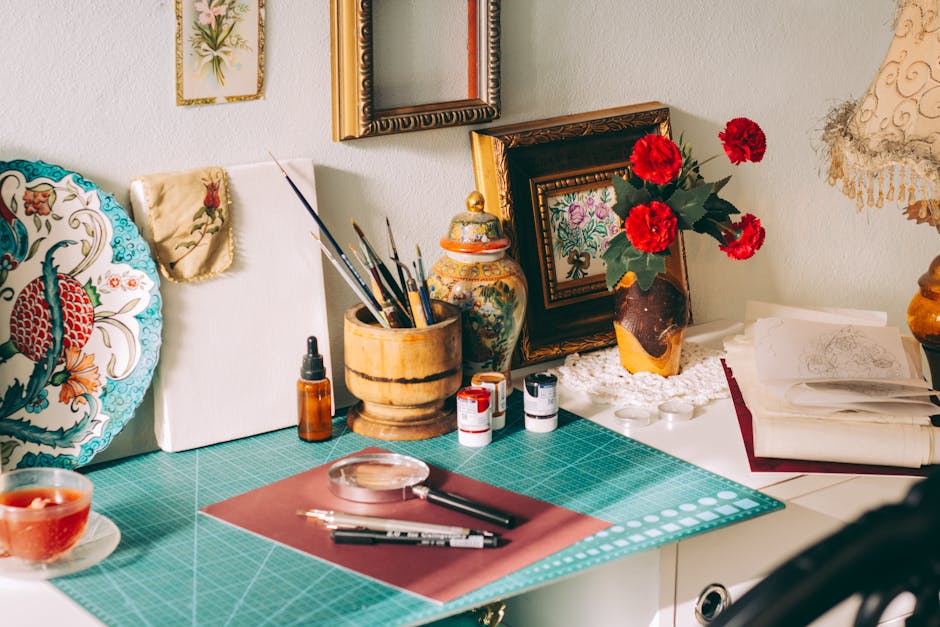 A cozy artist's workspace featuring painting supplies, decor, and floral accents on a desk.